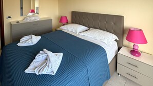 A hotel room with a bed, a bedside table with a lamp, a mirror, and a dresser. - Cozy Modern Apartment with Sea View (Sarandë)