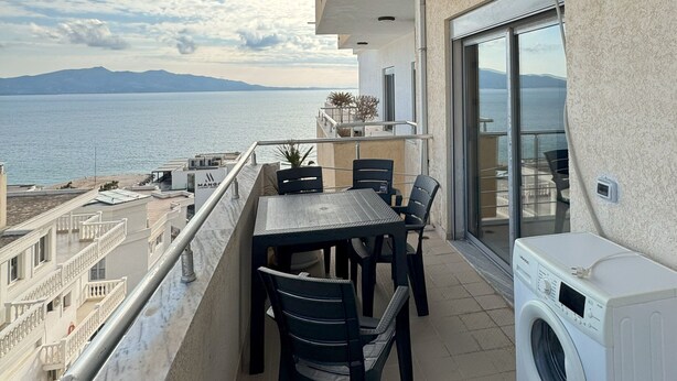 A balcony with a table and chairs, a washing machine, and a view of the sea and mountains. - Cozy Modern Apartment with Sea View (Sarandë)