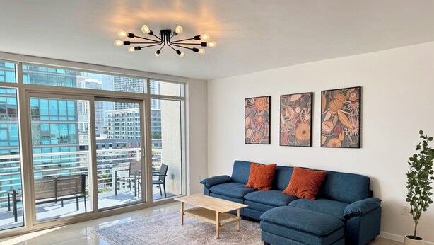A modern living room with a sectional sofa, a coffee table, and a large window offering a city view. - Spacious Midtown Miami 2-Bedroom Suite with Bay View (Miami)