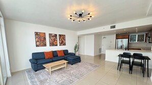A spacious living area with a blue sofa, a wooden coffee table, and a patterned rug. There is a dining area with black chairs and a kitchen with modern appliances. - Spacious Midtown Miami 2-Bedroom Suite with Bay View (Miami)