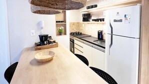 A modern kitchen with a wooden table, hanging light fixture, white refrigerator, and black chairs. - Csq Jardins By DayByDay (Joao Pessoa)