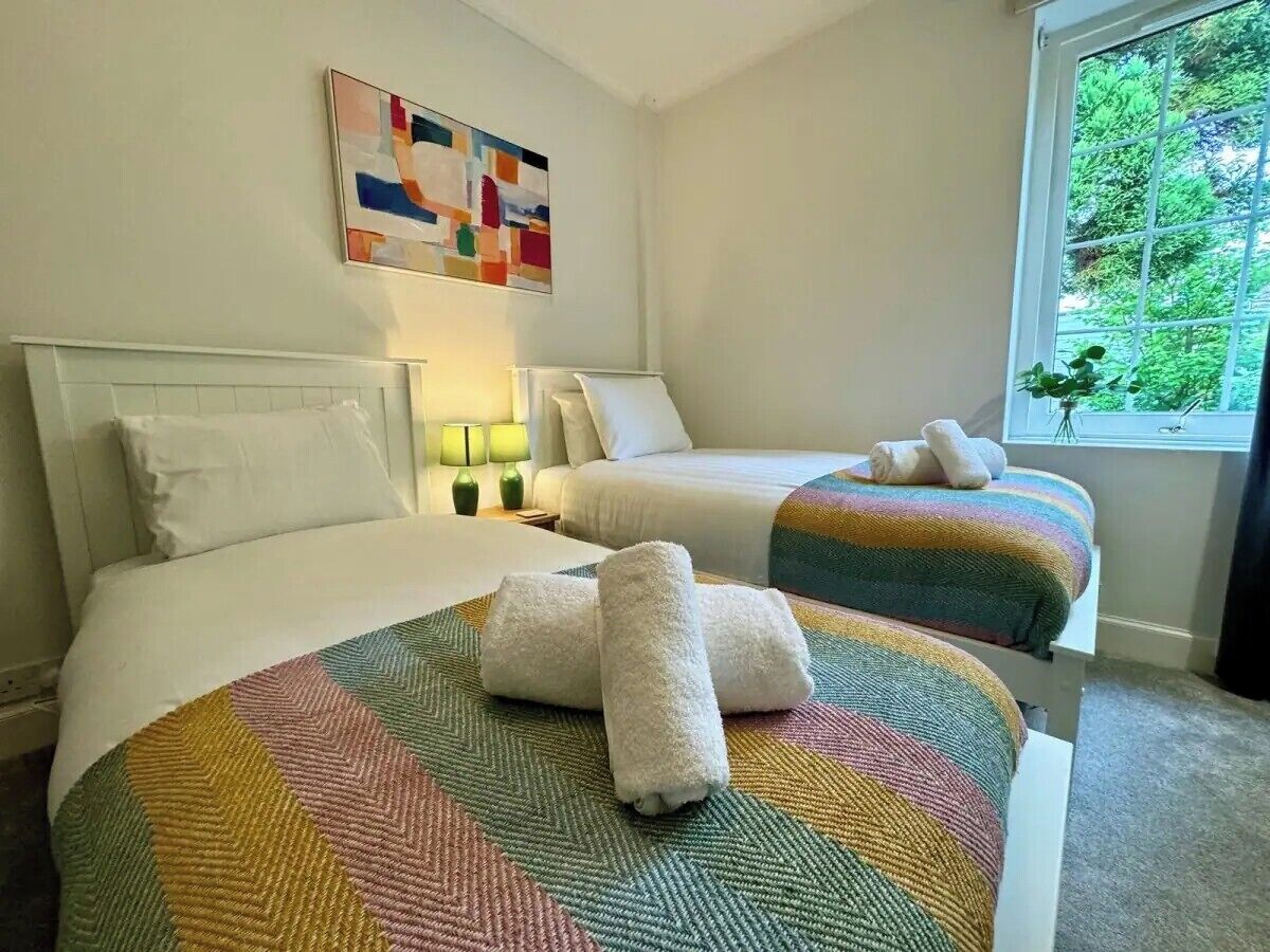 Habitación de hotel con dos camas, un colcha colorida y ventana con vistas a la vegetación.