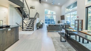 A modern living room with a staircase, a dining area, and large windows. - Modern Mountain Getaway Near Park City | Sleeps 15 (Park City)
