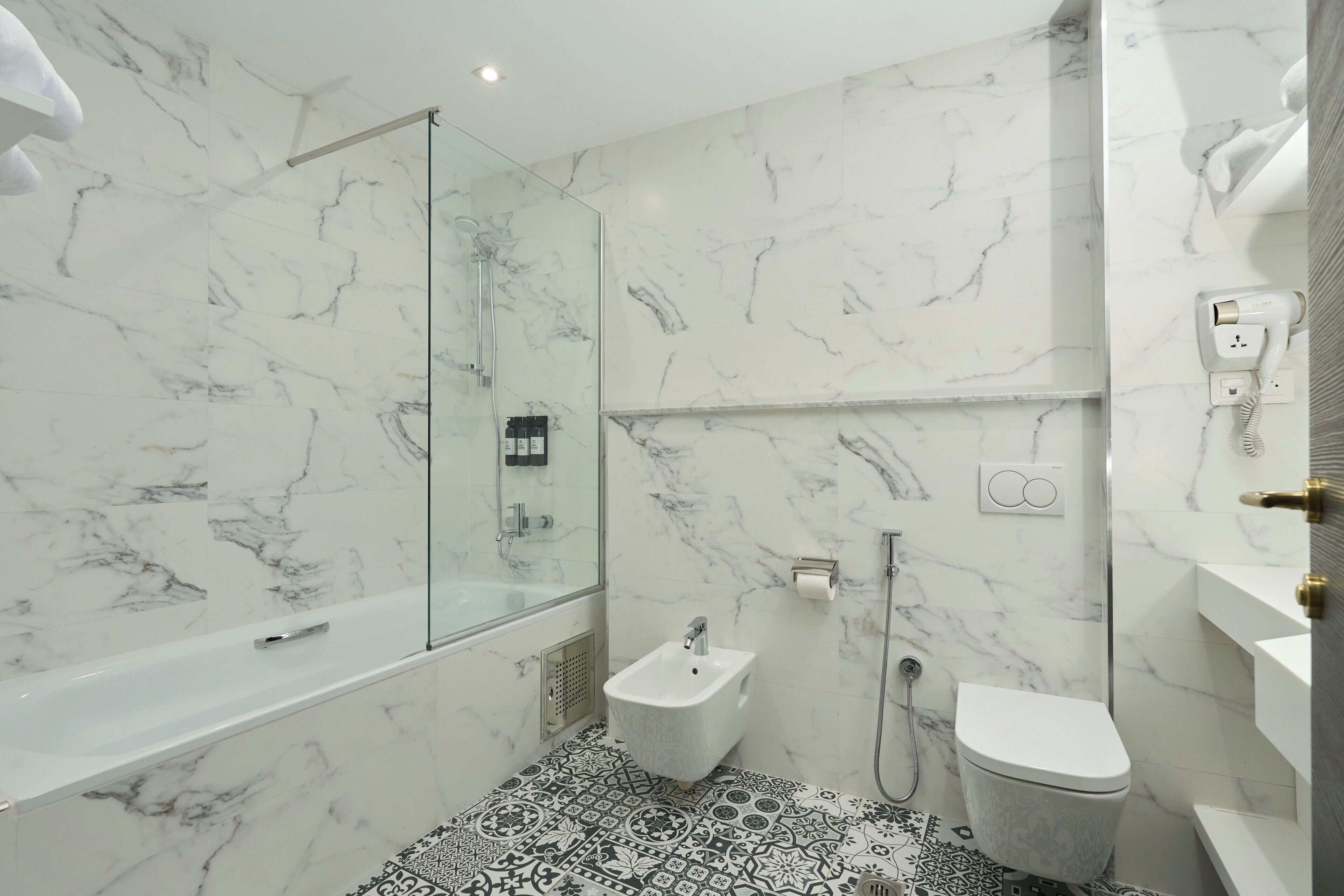 A modern bathroom with a marble floor, a glass-enclosed shower, a bidet, and a toilet.
