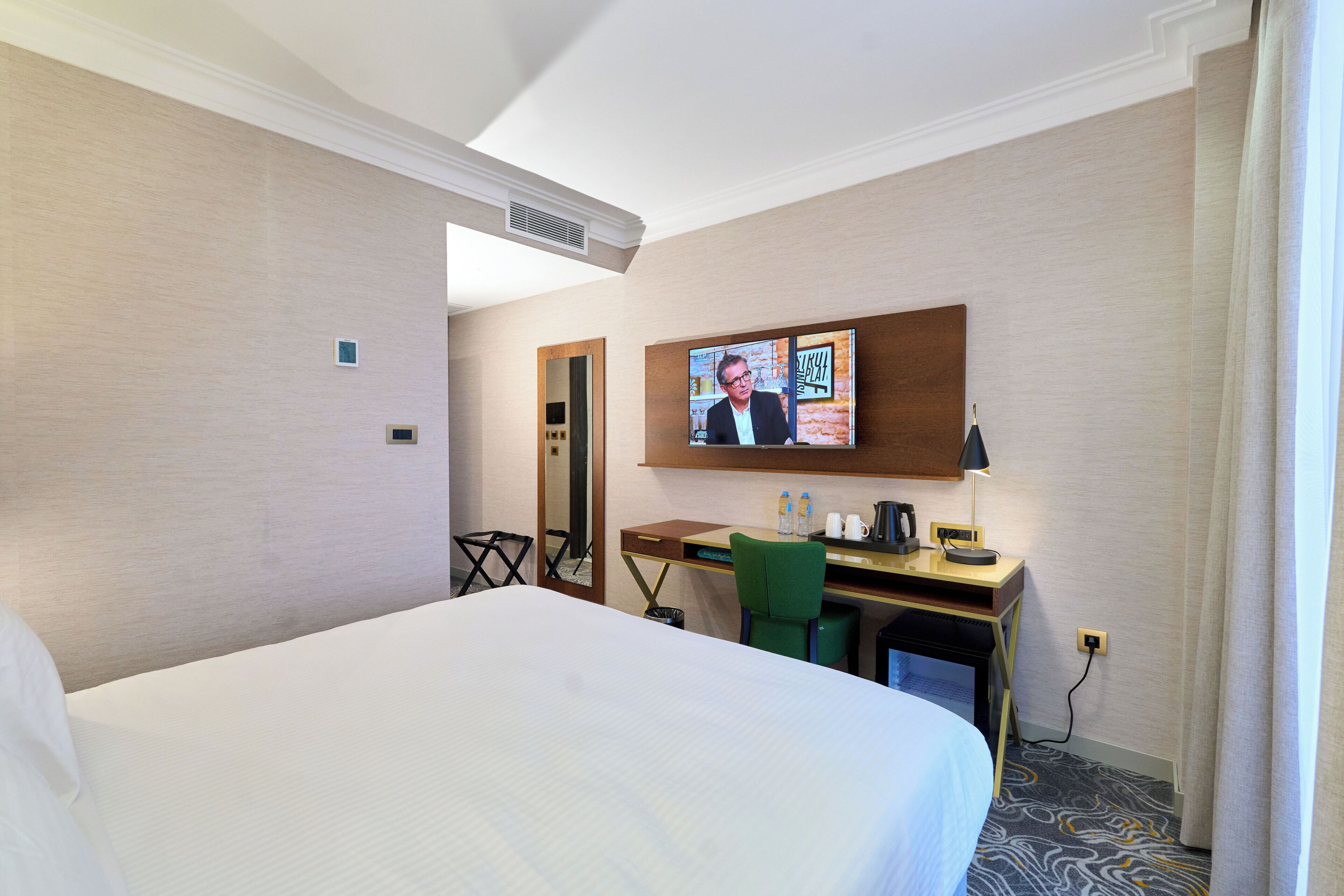 Habitación de hotel con una cama grande, un escritorio con computadora, una silla, televisor y un espejo.