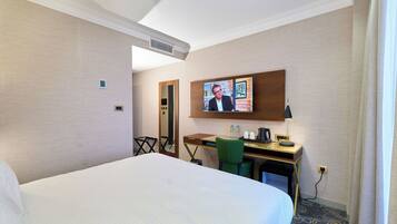 Habitación de hotel con una cama grande, un escritorio con computadora, una silla, televisor y un espejo.