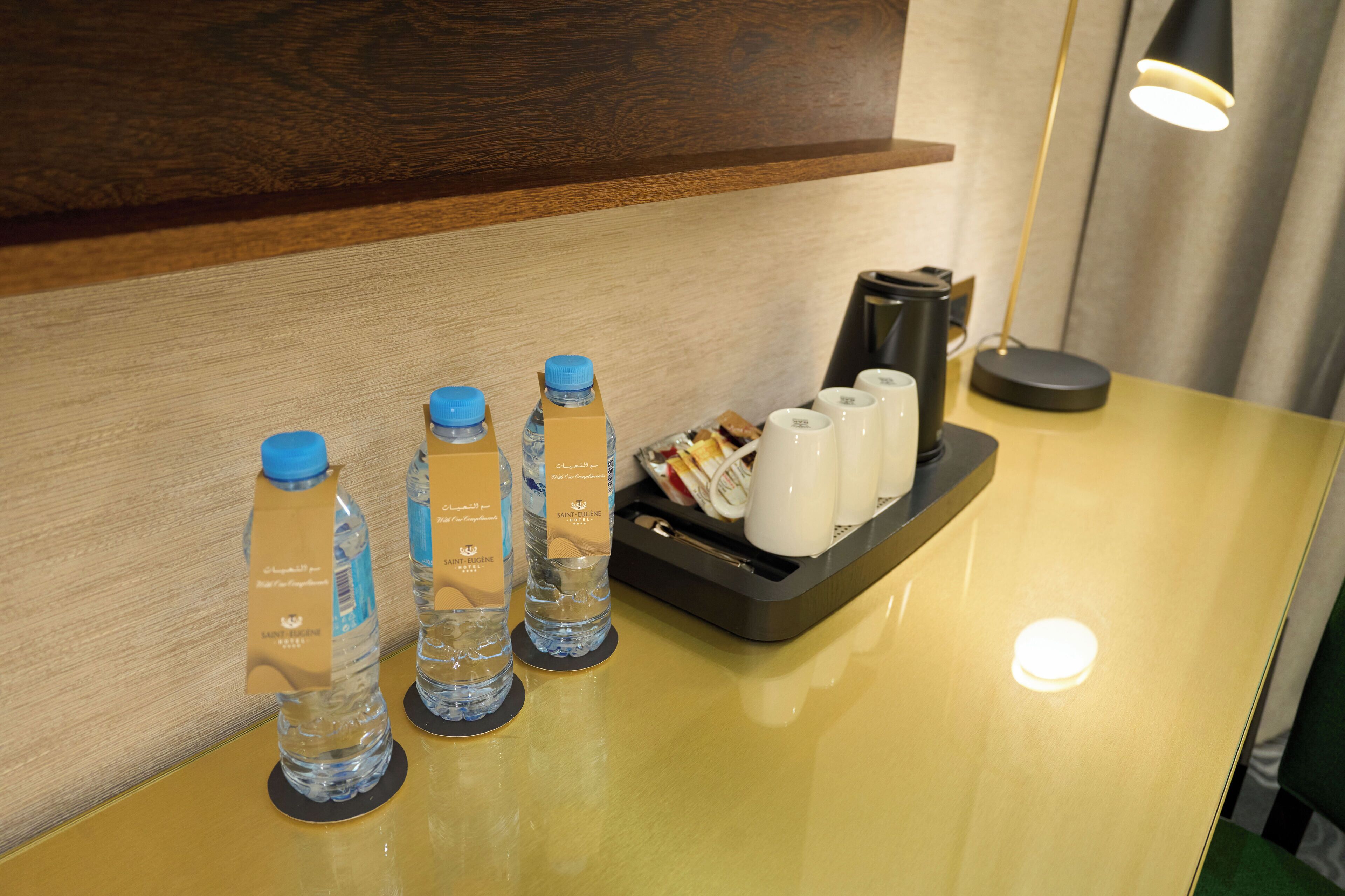 Zona de recepción de un hotel con un mostrador de madera, botellas de agua, una bandeja con tazas y una cafetera.
