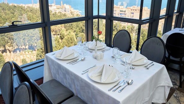 A dining table set for two with a white tablecloth, silverware, and glasses, overlooking a scenic view of the sea and greenery. - Hôtel St. Eugène (Algiers)