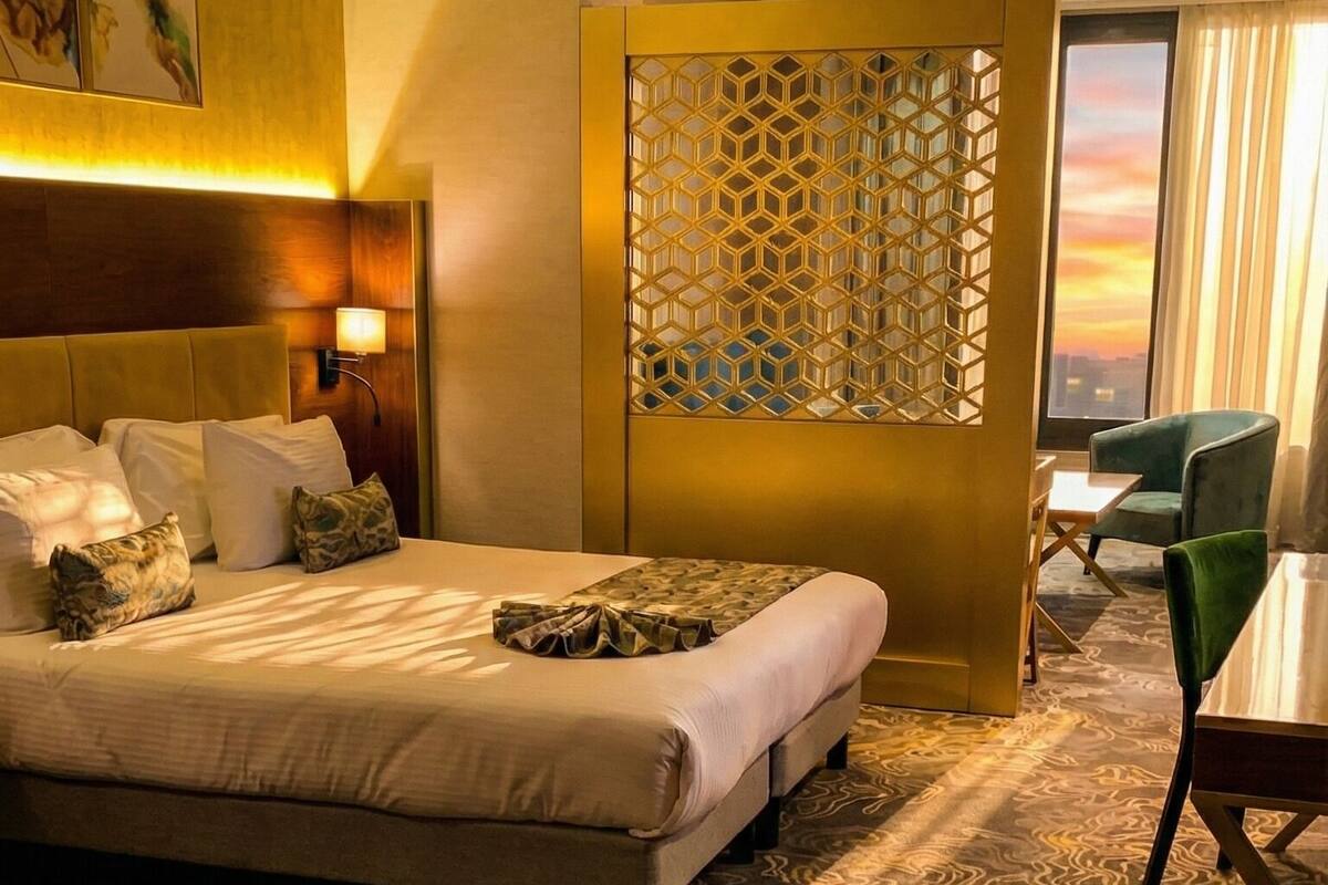 A hotel room with a large bed, a desk, a chair, and a view of the sunset through the window.