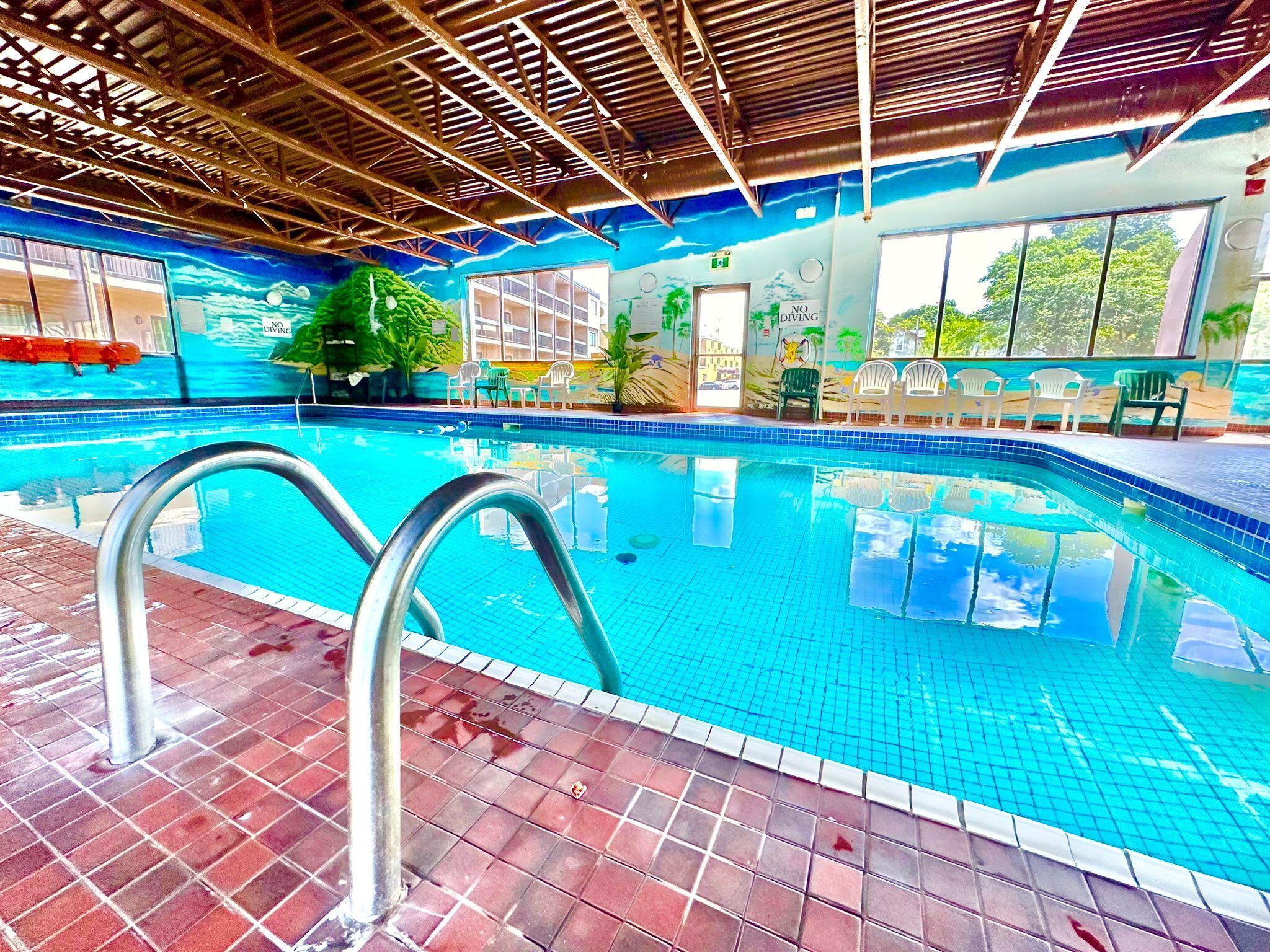 Ein beheiztes Hallenbad mit klarem, blauem Wasser, einer Metallleiter und einem gefliesten Boden.