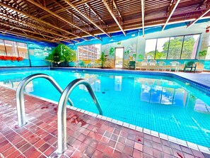 Una piscina interna con acqua cristallina, una scala di metallo e un pavimento piastrellato.