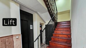 Eine Holztreppe mit schwarzer Geländer führt zu einer Tür mit der Aufschrift 'Lift'.