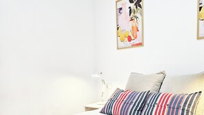 Ein ordentlich bezogenes Bett mit weißer Bettwäsche, einer roten Decke und gestreiften Kissen.