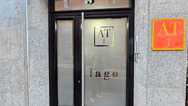 Ein Gebäudeeingang mit einer Glastür, auf der "AT Lago" steht und darüber die Zahl "3" angebracht ist.