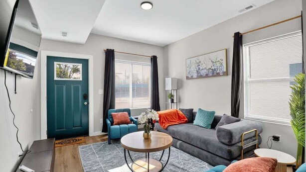 Ein modernes Wohnzimmer mit einer Couch, Sesseln, einem Couchtisch und einem an der Wand befestigten Fernseher.