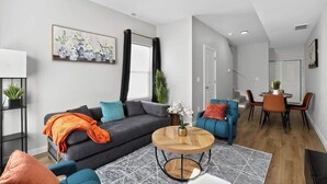 Ein modernes Wohnzimmer mit einem grauen Sofa, blauen Sesseln, einem Holztisch und einem Essbereich mit Tisch und Stühlen.