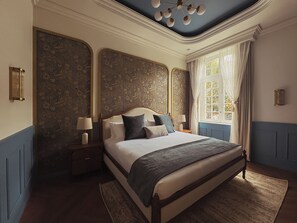A bedroom with a large bed, two bedside tables with lamps, a window with curtains, and a decorative ceiling light. - Roma Nueve Dos Hotel Boutique (Mexico City)