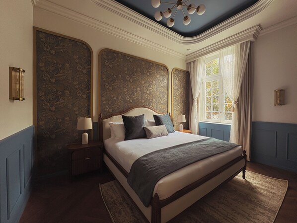 Une chambre à coucher avec un grand lit, deux tables de chevet avec des lampes, une fenêtre avec des rideaux et un luminaire décoratif au plafond.