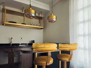 Une cuisine dotée d’un coin bar, de luminaires suspendus et d’une fenêtre ornée de rideaux légers.