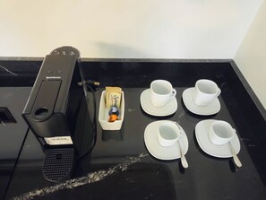Une machine à café Nespresso, quatre tasses et sous-tasses blanches, une boîte de capsules de café Splendid et une petite bouteille orange.