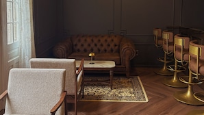 Une pièce comprenant un canapé capitonné, des chaises à motifs, une petite table, un tapis à motifs et des tabourets de bar.