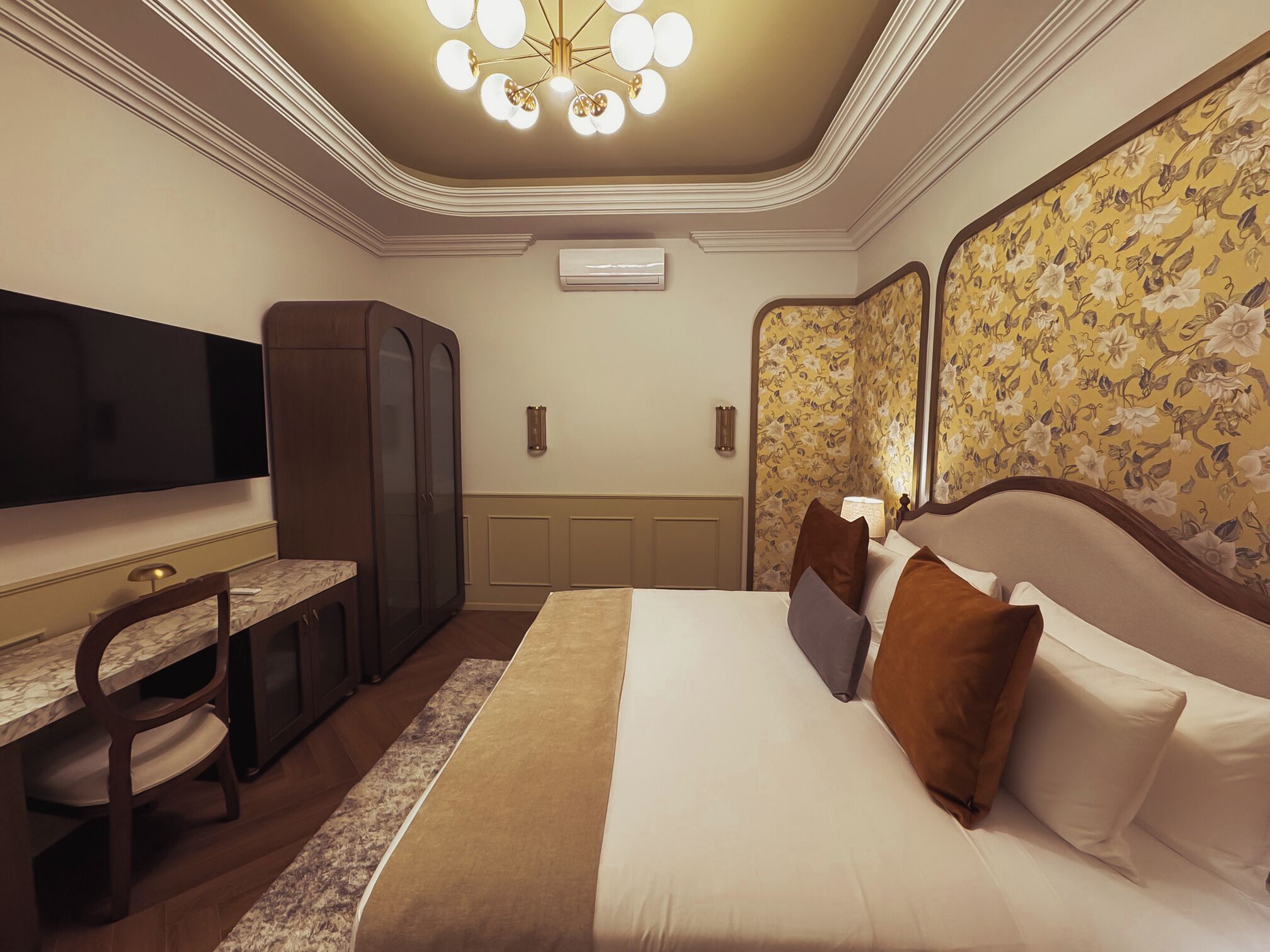Une chambre d’hôtel comprenant un lit, un bureau, une télévision, une armoire et un mur décoratif.