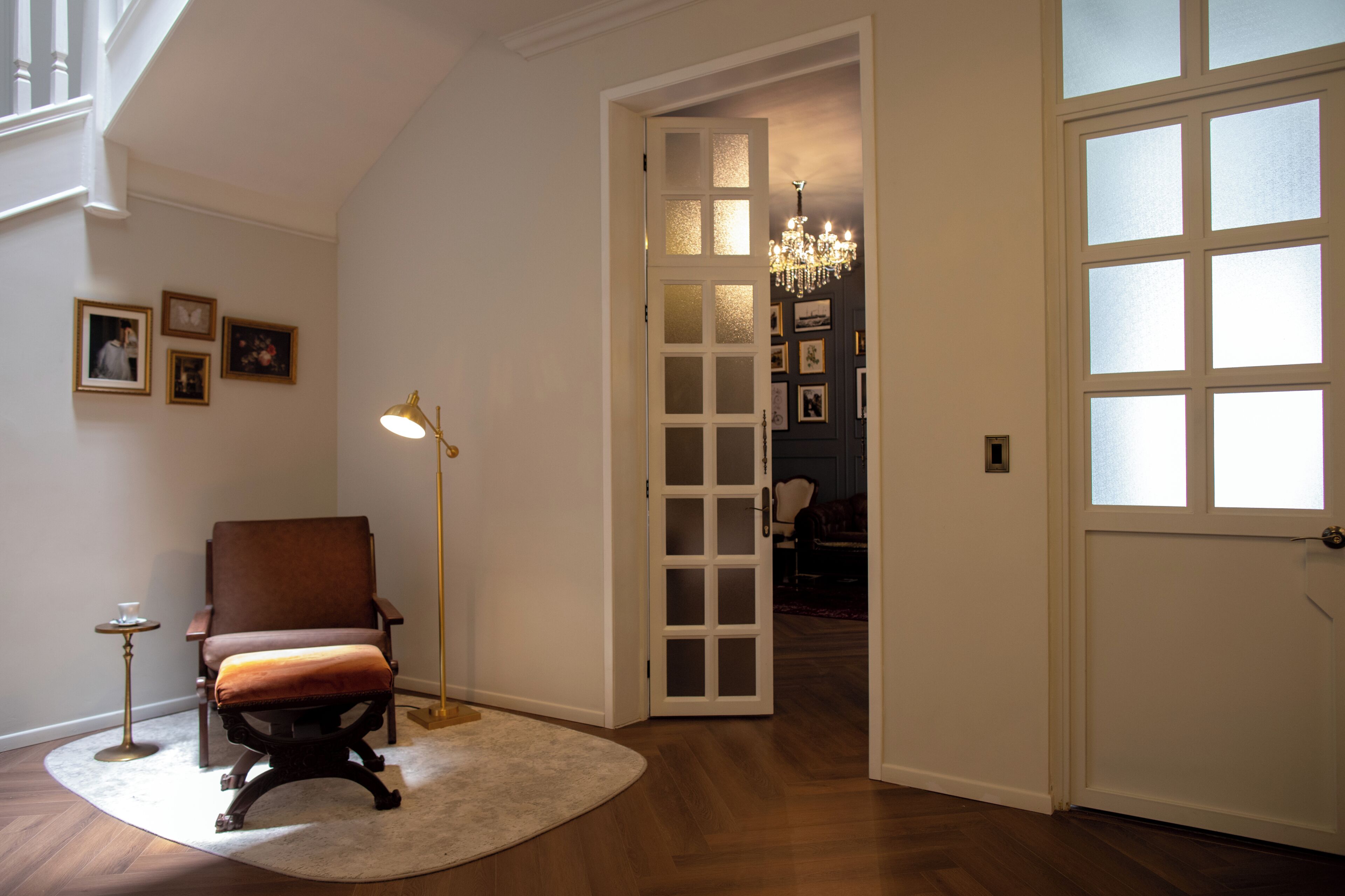 A room with a chair, a floor lamp, a door, and a chandelier.