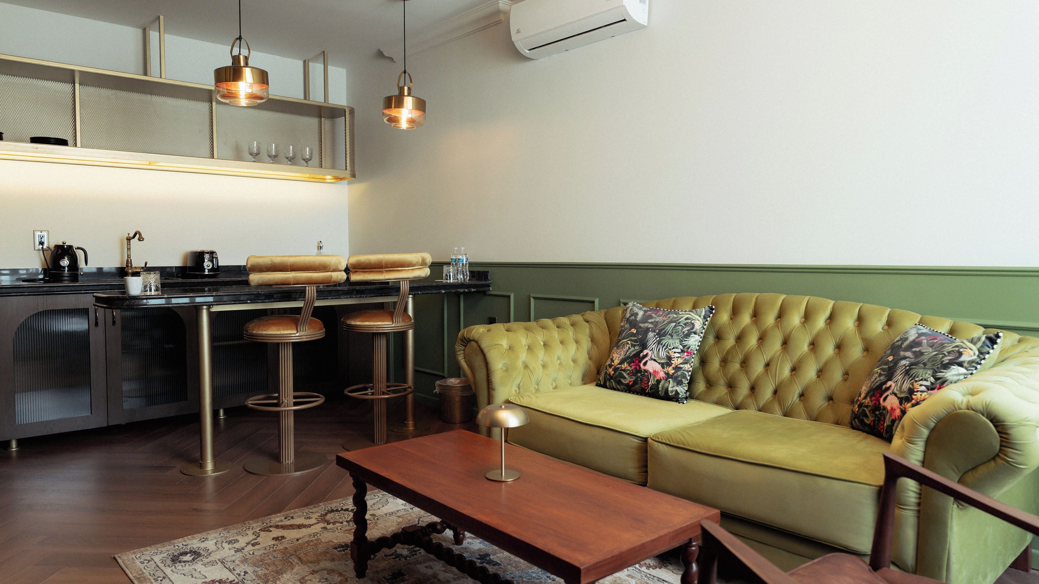 Un salon moderne avec un canapé vert recouvert de tissu, une table basse en bois et un coin cuisine doté de tabourets de bar.