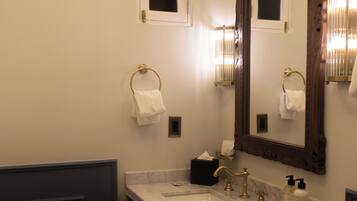 A bathroom with a marble sink, gold faucets, a large mirror, and two towel rings.