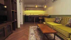 Ein gemütlicher Wohnbereich mit Sofa, Couchtisch, Fernseher, Küchenzeile und einem gemusterten Teppich.