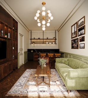 A living room with a green sofa, a wooden coffee table, a chandelier, and a kitchen area with a marble countertop. - Roma Nueve Dos Hotel Boutique (Mexico City)