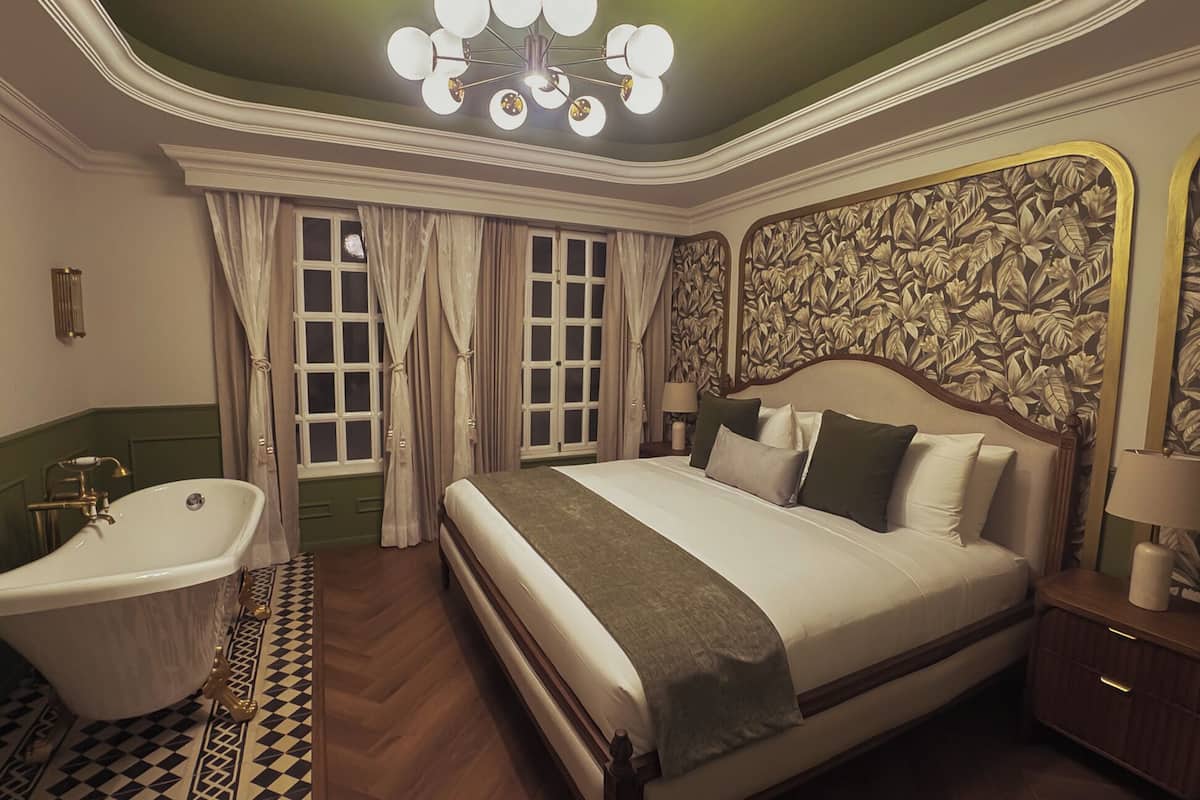 A bedroom with a large bed, a classic bathtub, and a chandelier.