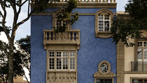 Ein Gebäude mit blauer Fassade, großen Fenstern und einem Balkon mit Beleuchtung.