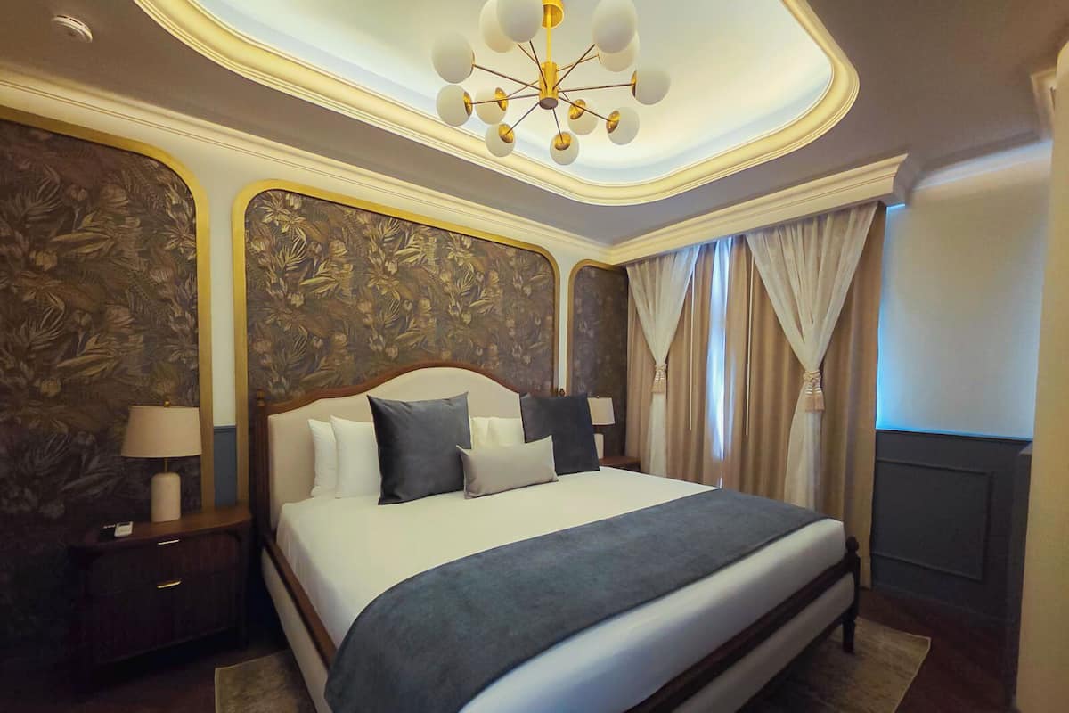 A large bed with a headboard, a nightstand, a lamp, and curtains.