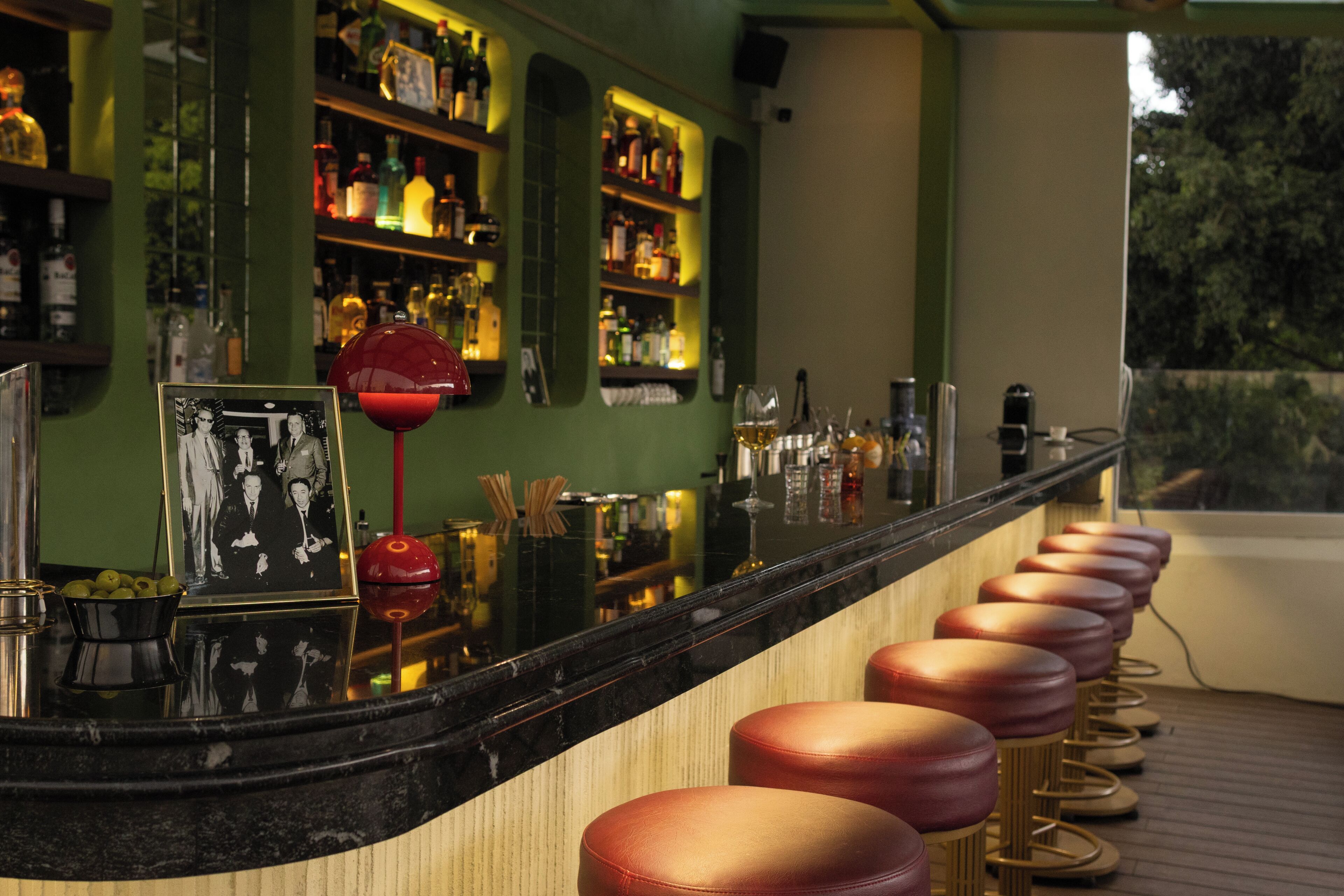 Un bar con una barra alargada, varias estanterías llenas de botellas y un cuadro enmarcado.