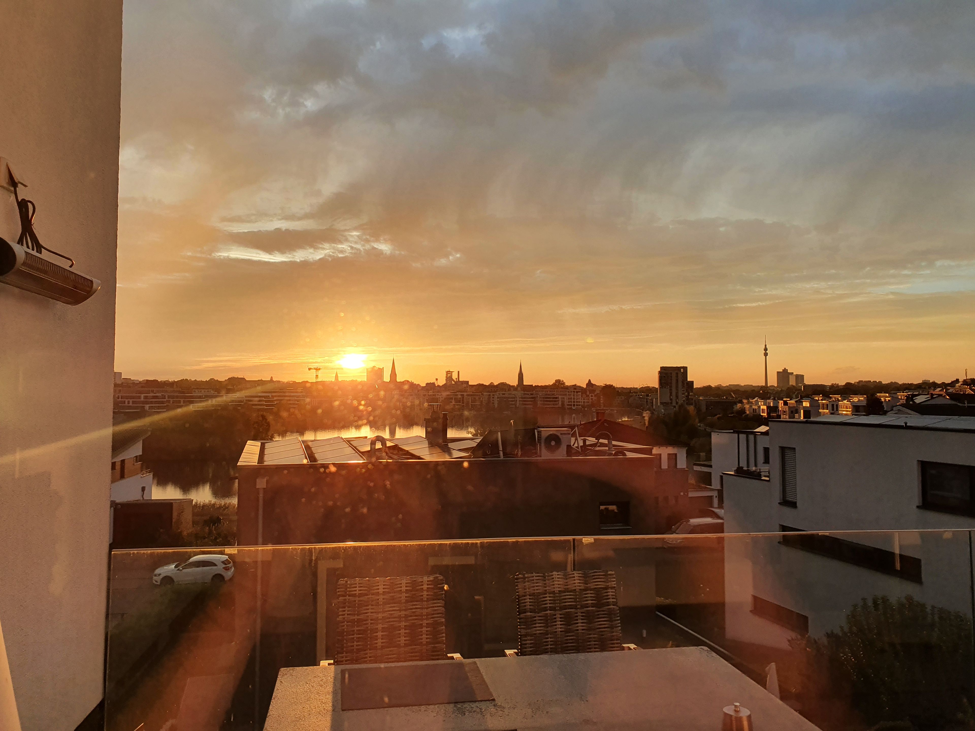 Ein Sonnenuntergangsblick von einem Balkon mit Blick auf eine Stadtlandschaft, Gebäude und einen Fluss.