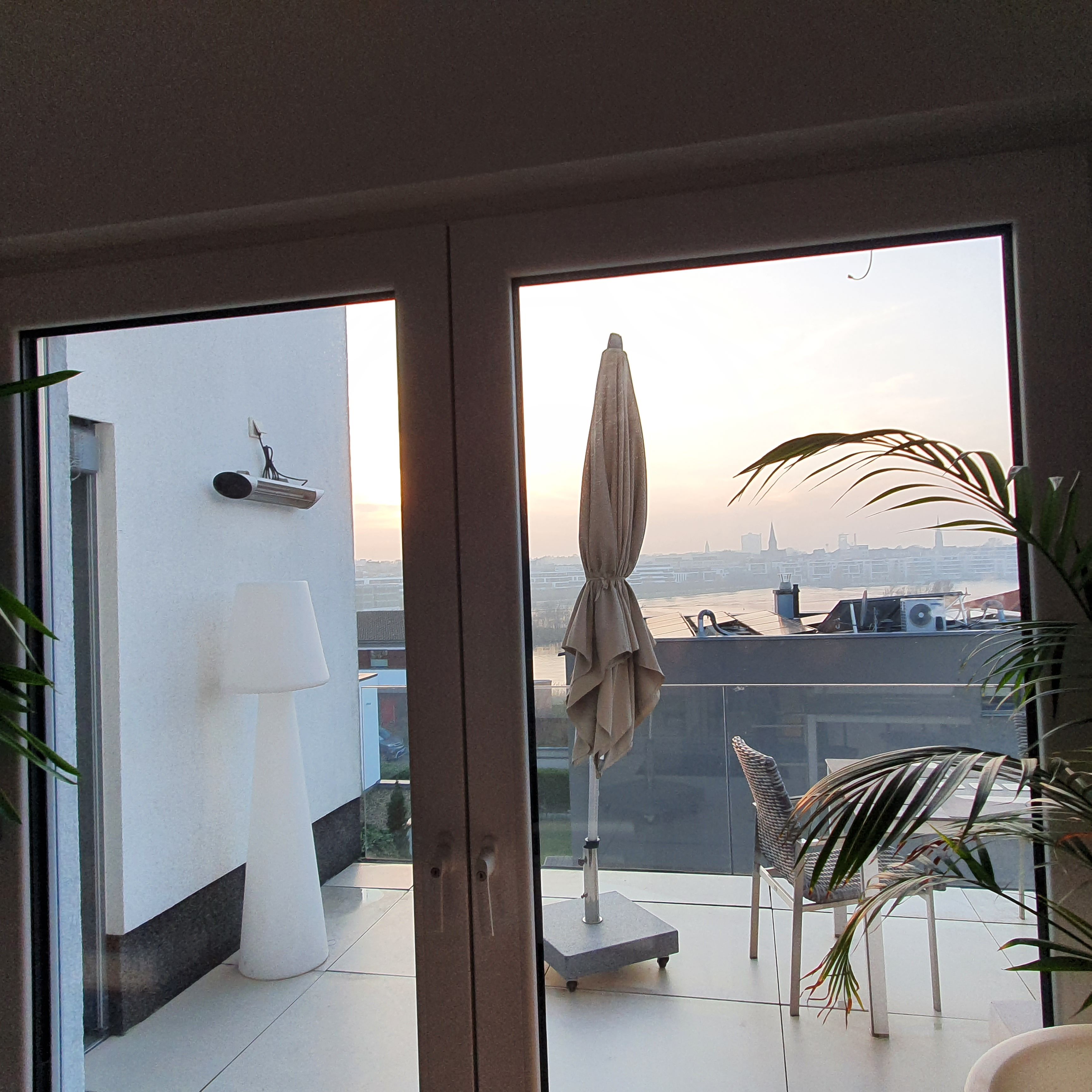 A balcony with a view of a city skyline, a table, chairs, and a potted plant.