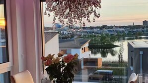 Spiseområde med et bord og stole, en vase med blomster og udsigt over en by med bygninger og et vandareal.