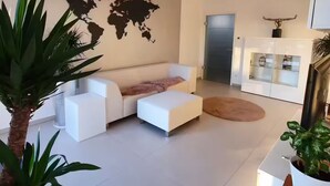 En moderne stue med en hvid sofa, et verdenskort på væggen og et køkkenområde med køleskab og skabe.