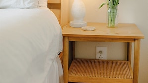 A bed with white bedding, a white lamp, and a vase with red flowers on a wooden nightstand.