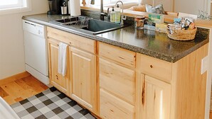 A kitchen with a dishwasher, a sink, a coffee maker, and a window with curtains.