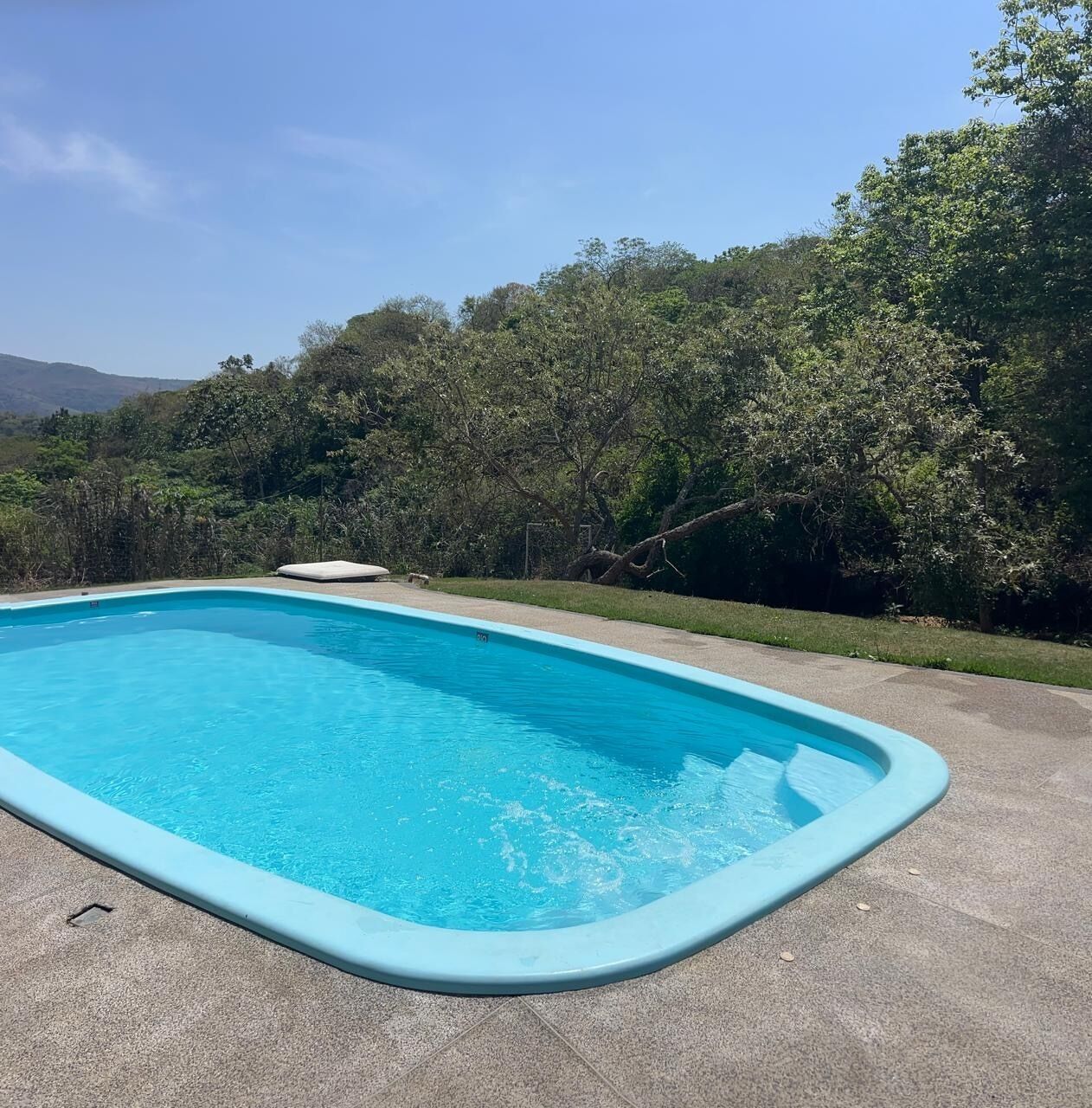 A rectangular swimming pool with a light blue edge, surrounded by a concrete deck.