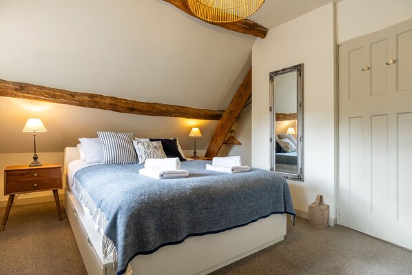 A bedroom with a bed, bedside lamps, a mirror, and a wooden ceiling beam.