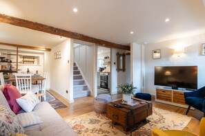 A spacious living room with a sofa, a coffee table, and a TV. A staircase leads to a kitchen and dining area.