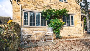 Ein Steinhaus mit einer kleinen Terrasse, auf der ein Tisch und zwei Stühle stehen.