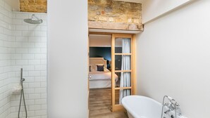 A bathroom with a shower, a bathtub, and a wooden door leading to a bedroom. - Stunning 4-Bedroom Barn Conversion (Sulgrave)
