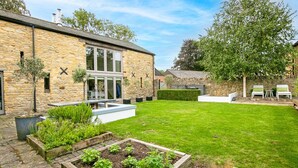 A stone building with a modern glass extension, a well-maintained lawn, and outdoor seating. - Stunning 4-Bedroom Barn Conversion (Sulgrave)