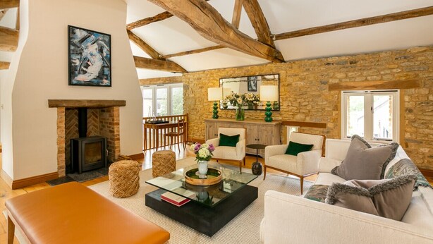 A rustic living room with exposed wooden beams, a stone wall, a fireplace, and comfortable seating. - Stunning 4-Bedroom Barn Conversion (Sulgrave)