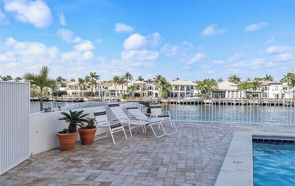 A poolside area with lounge chairs and potted plants, overlooking a marina with boats and palm trees. - Beach Front Bliss in Hollywood (Hollywood)