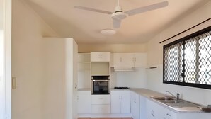 Una cocina con armarios blancos, una estufa y un ventanal con mosquitero.